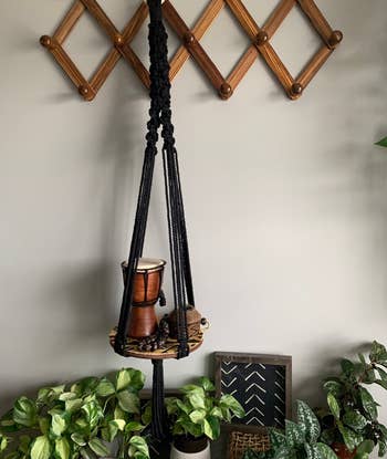 Macrame plant hanger holding a pot, against a wall with a diamond pattern rack and plants on the side
