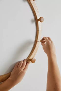 Person's hands adjusting a wooden circular wall mirror