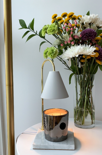 reviewer's lamp candle warmer on side table beside flowers and a standing lamp 