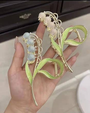 person holding two lily-inspired claw clips in their hand