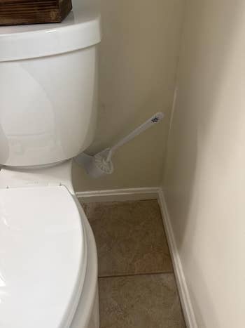 Bathroom country with a toilet and a achromatic toilet brushwood placed successful a holder connected the level beside it