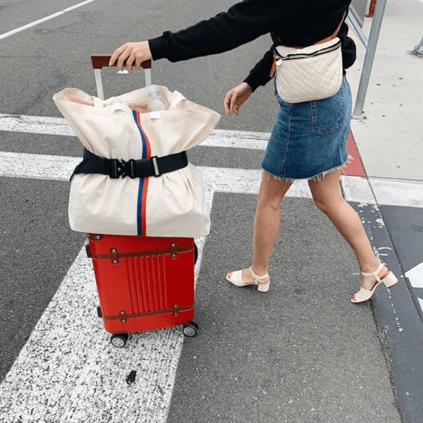 A model pushing their luggage with a bag attached to the top with a strap