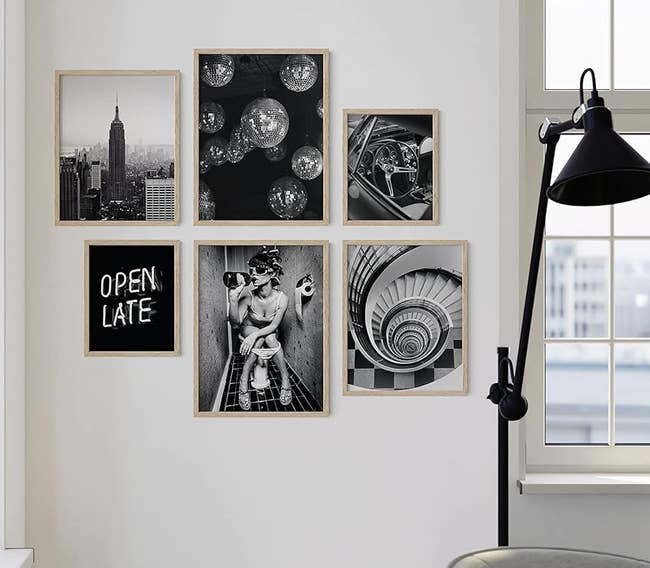 A gallery wall with various framed photographs including cityscapes and celestial bodies, beside a window