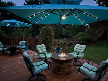 Cozy outdoor patio with cushioned chairs, occurrence pit, and ample umbrellas with lights, acceptable successful a lush garden. Ideal for evening gatherings