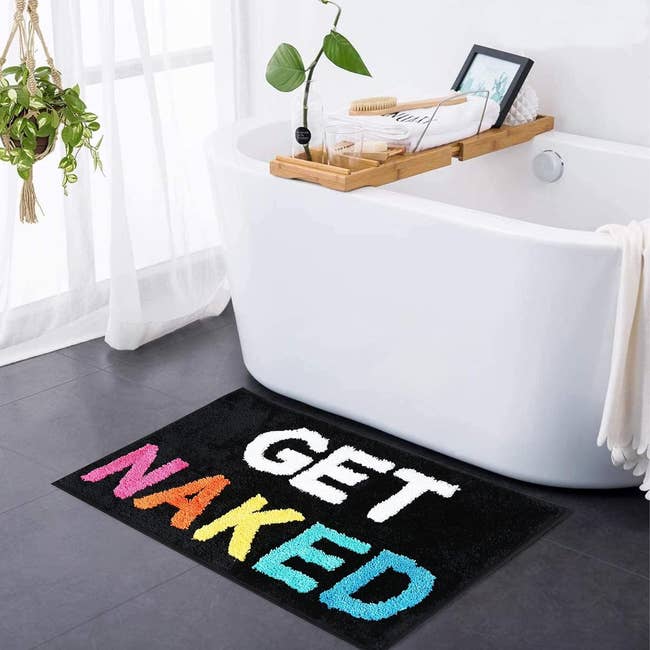 black bath mat with colorful lettering that says get naked
