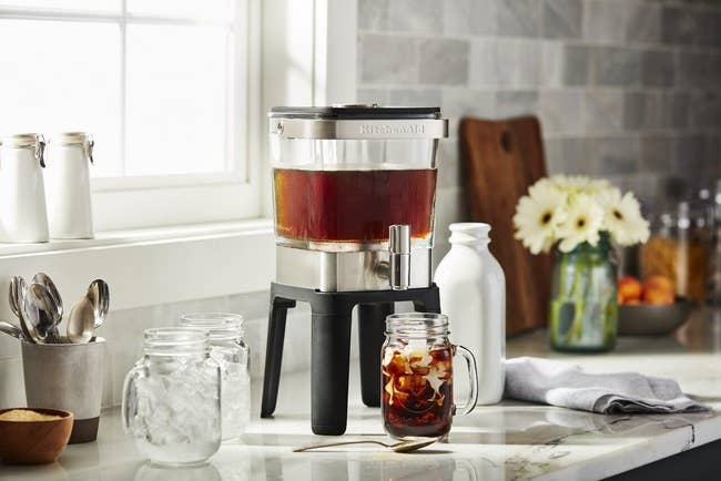 stainless steel cold brew maker next to a glass of iced coffee