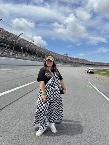 Person connected a racetrack wearing a checkered formal and graphic T-shirt, with a headdress featuring a logo. Stadium seating and way visible