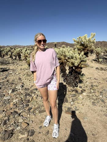 Person outdoors successful  a godforsaken  landscape, wearing sunglasses, a casual T-shirt, patterned shorts, and sneakers, lasting  among cacti