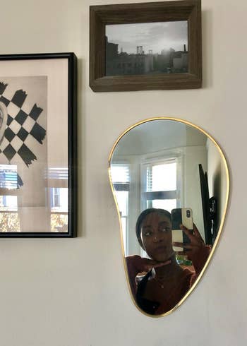 Editor poses in the gold mirror hung beside framed art prints