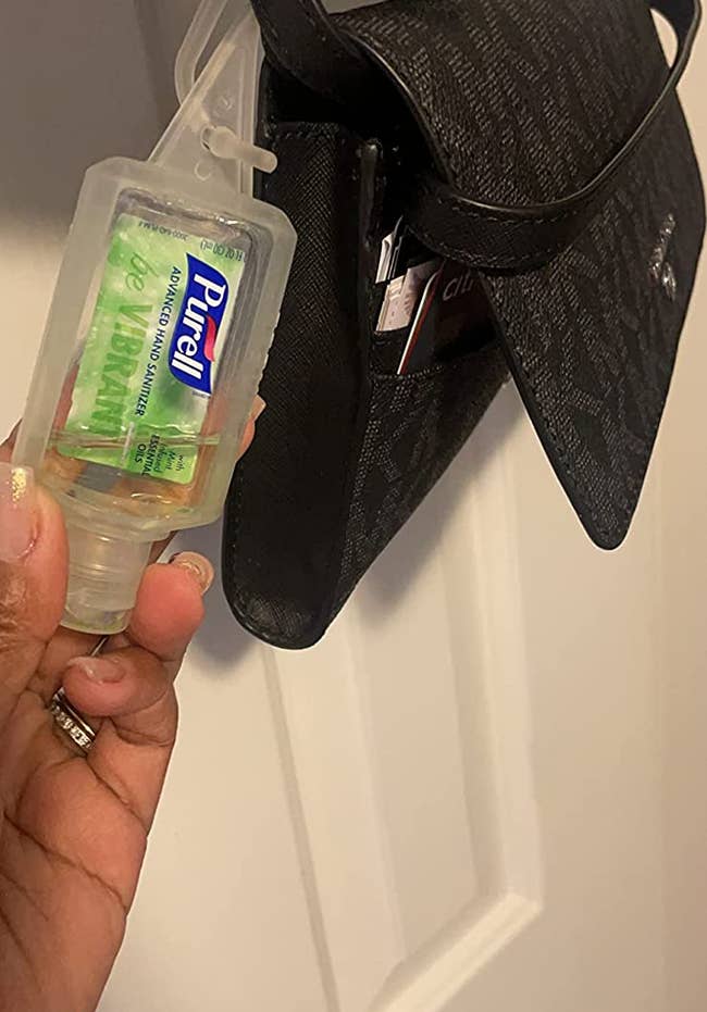 reviewer holding the green travel bottle of hand sanitizer, which is clipped onto the handle of a small black bag