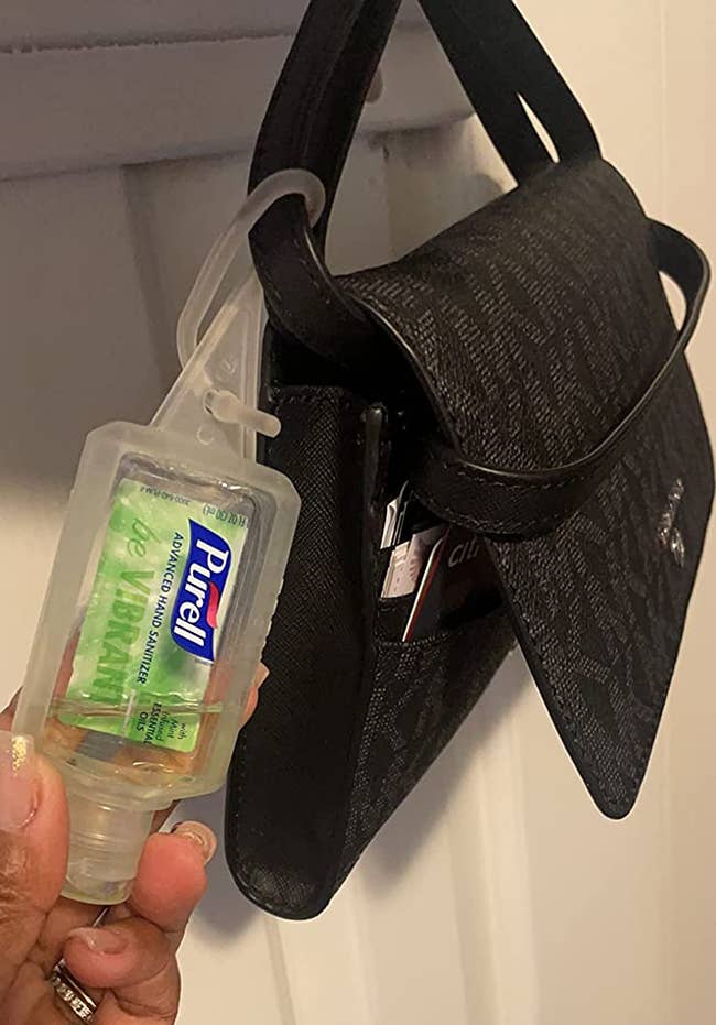 reviewer holding the green travel bottle of hand sanitizer, which is clipped onto the handle of a small black bag