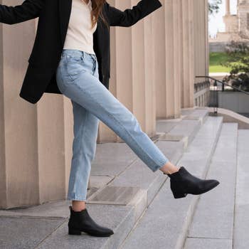 Person in a black blazer and jeans showcasing ankle boots. Suitable for a shopping article on footwear