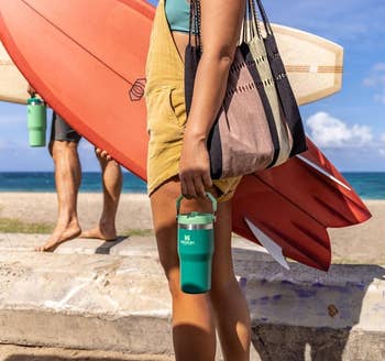 the model holding the water bottle in one hand and a surfboard in the other