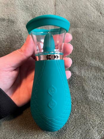 Reviewer holding a green portable, textured silicone suction vibrator with buttons