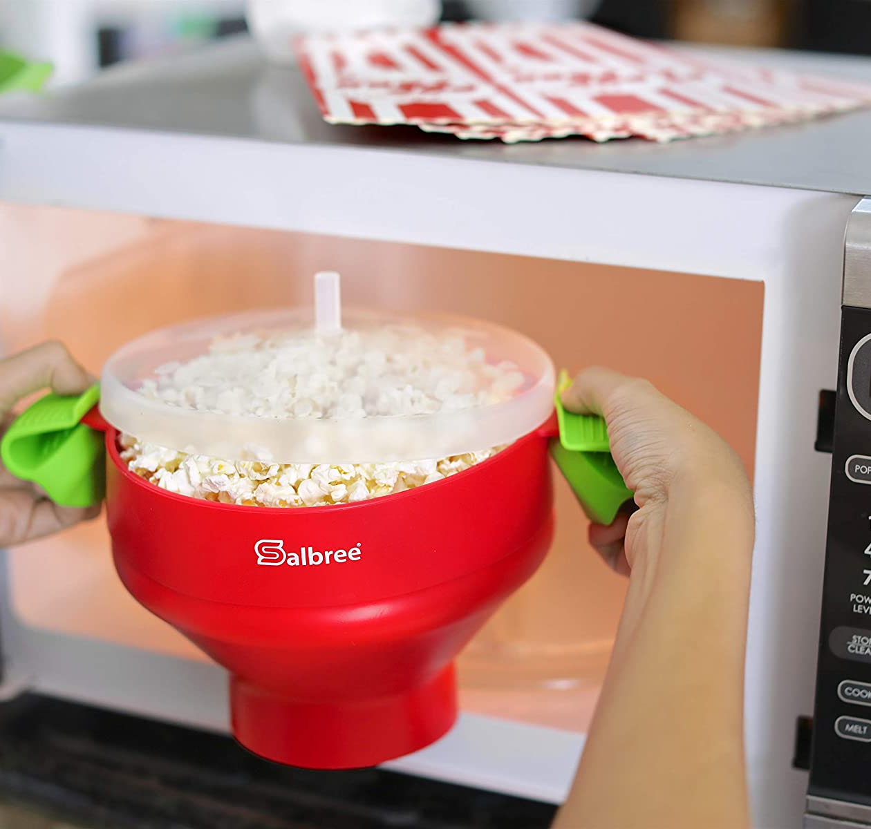 hands taking a red popcorn maker filled with popcorn out of a microwave