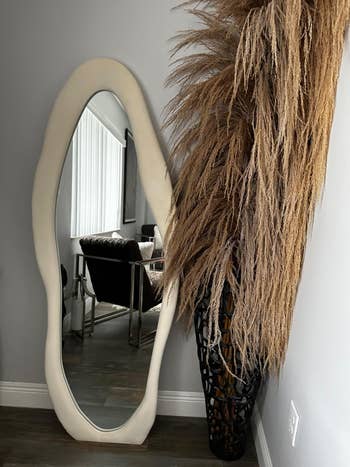 Full-length mirror beside a textured decor item in a modern interior setting, reflecting a home office space