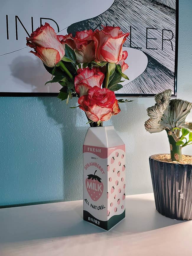 strawberry milk carton vase with flowers in it sitting on reviewer's shelf