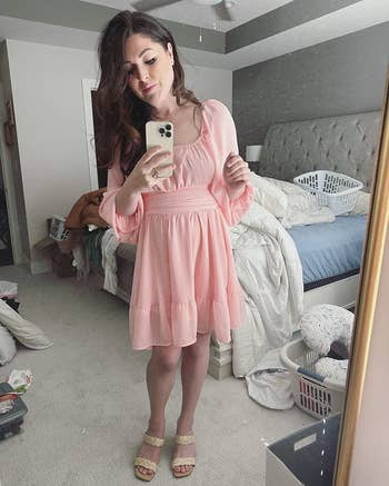 Person taking a mirror selfie wearing a casual, pastel dress and strapped sandals
