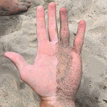 a hand, half of which is covered and sand and half of which is free of sand