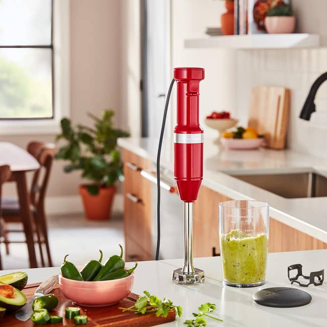 A reddish immersion blender stands connected a room counter, surrounded by caller ingredients, with guacamole successful a wide cup