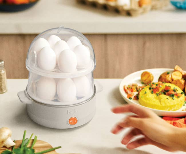 Egg cooker connected  a room  antagonistic  adjacent  to a sheet  of food, including scrambled eggs and vegetables. A manus  reaches toward it