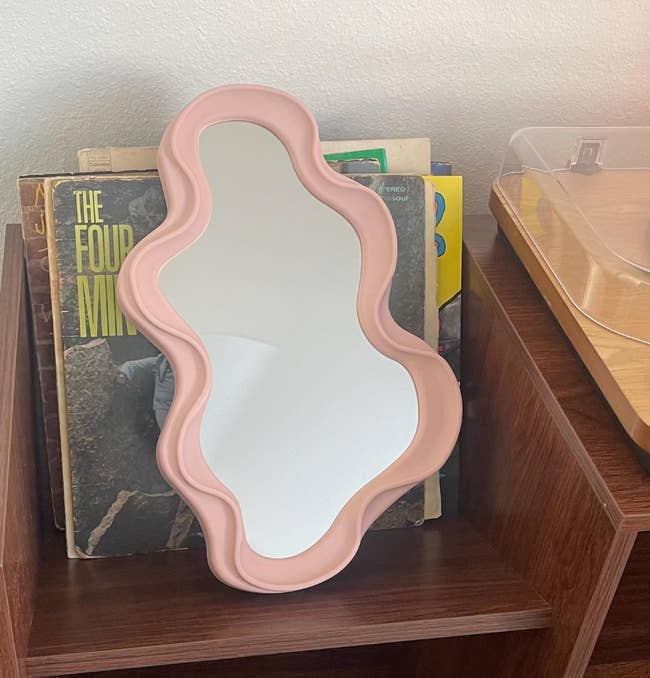 Wavy-edged mirror on a wooden shelf with books in the background