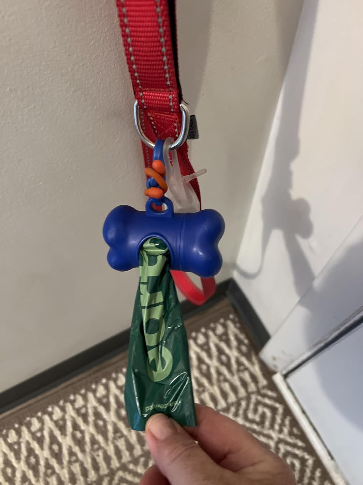 A bone-shaped canine  discarded  container  holder with a greenish  container  hangs from a reddish  leash connected  a hook