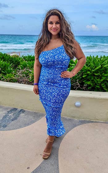 reviewer in a blue floral dress standing by the beach, hand on hip