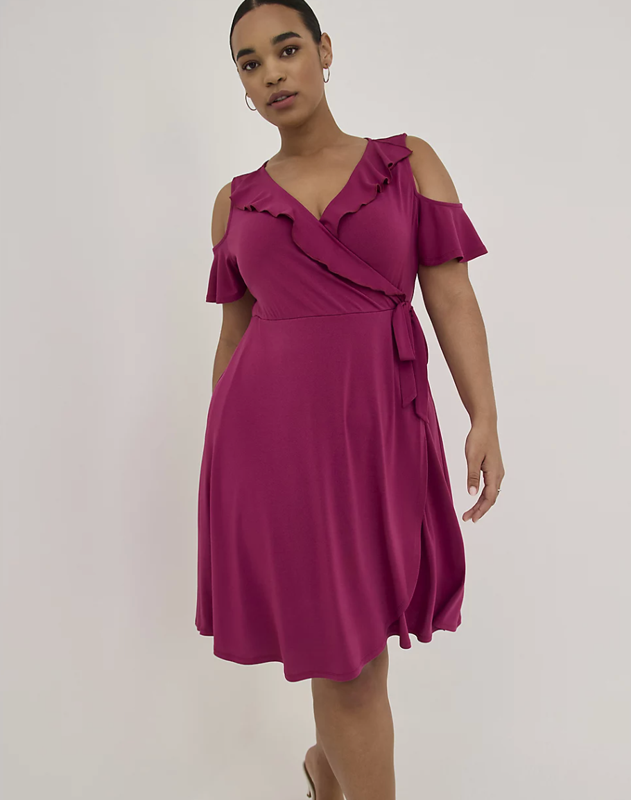 Model is wearing a pink wrap dress with cold shoulders