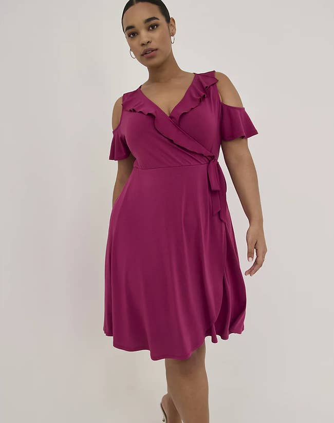 Model is wearing a pink wrap dress with cold shoulders