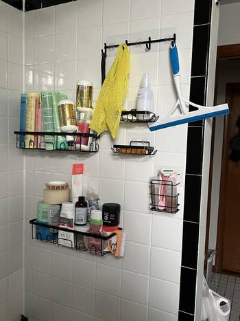 Bathroom shelves filled with various hair and body products, a squeegee, and a yellow washcloth hanging on hooks