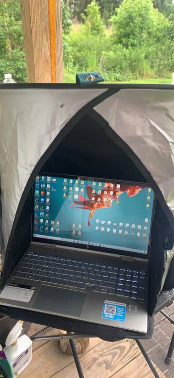 Laptop with icons on the screen under a shaded enclosure outdoors. Environment shows vegetation in the background