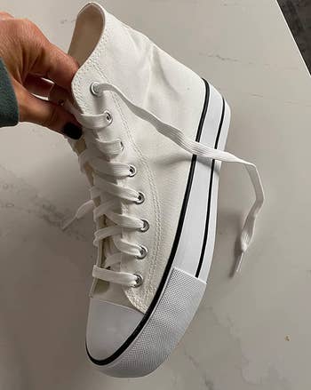 Reviewer holding a white high top laced sneaker 
