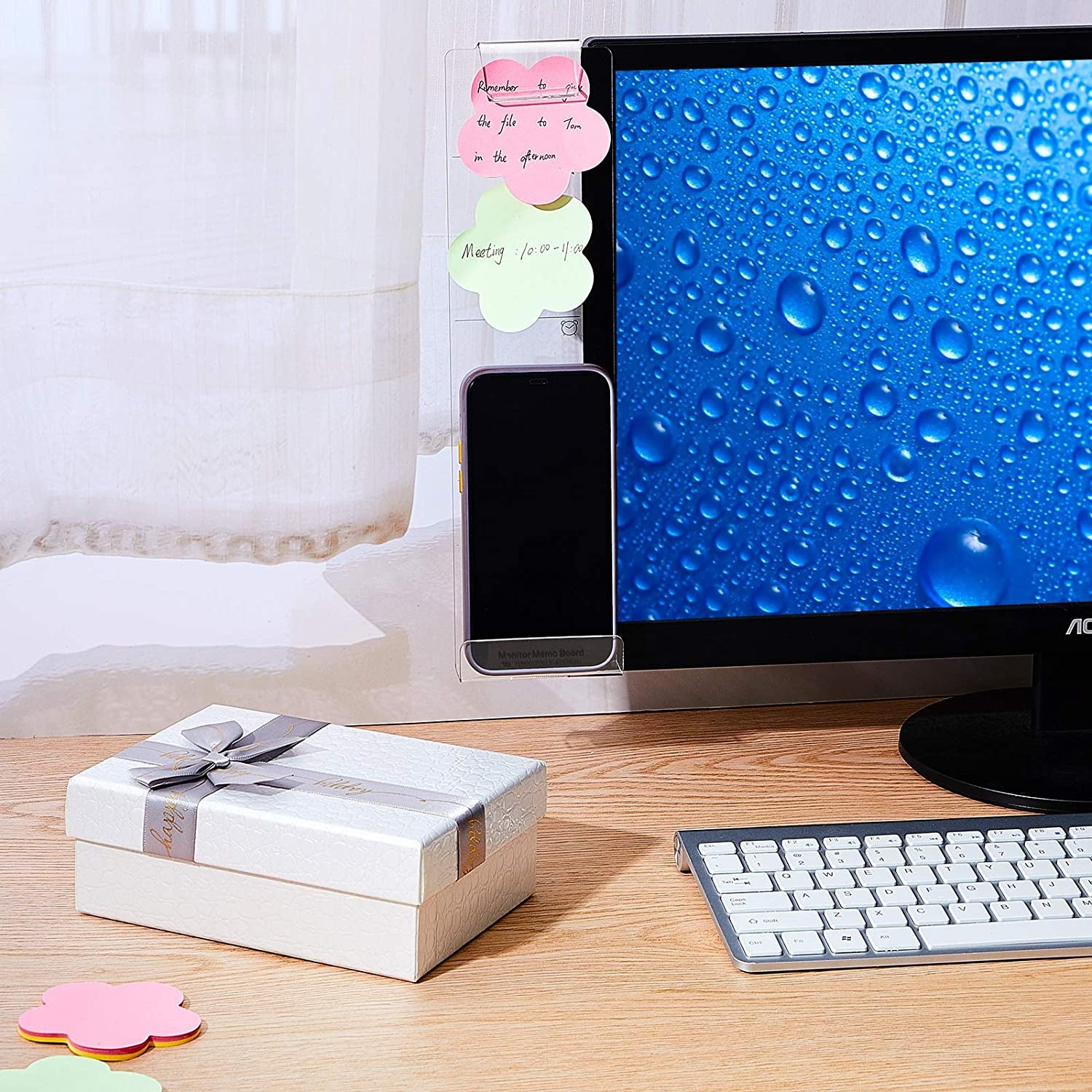 Clear plastic memo board attached to a computer monitor with a photo, two sticky notes and a lip with a cell phone on it