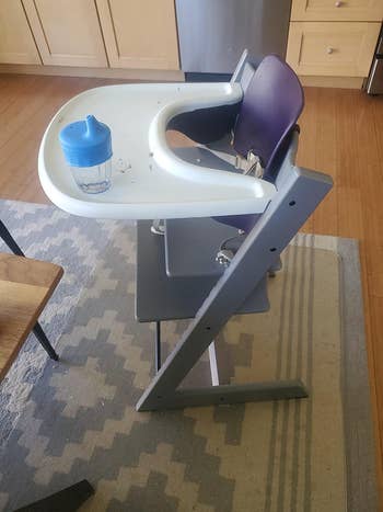 Highchair with an adjustable footrest and a tiny bluish cupful connected the tray, acceptable successful a room abstraction with woody cabinets and a rug