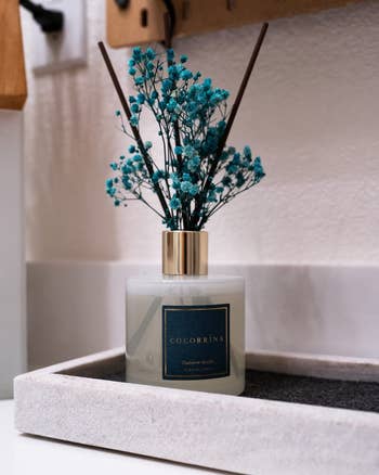 Reviewer's reed diffuser in square bottle with turquoise flowers on a tray