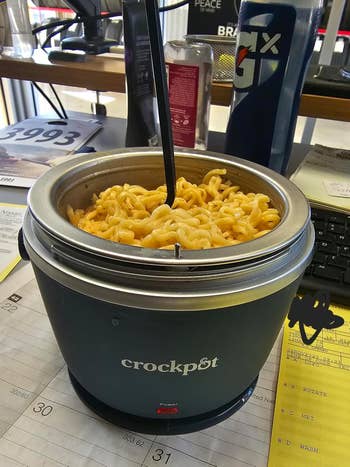 Close-up of noodles in a reviewer's Crock-Pot on an office desk, with a fork in the pot