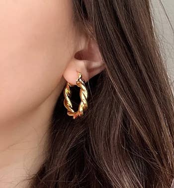 Close-up of a person wearing a chunky gold hoop earring