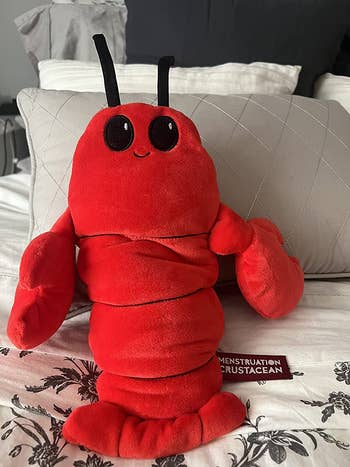 reviewer photo of the red plush lobster heating pad leaning against a pillow