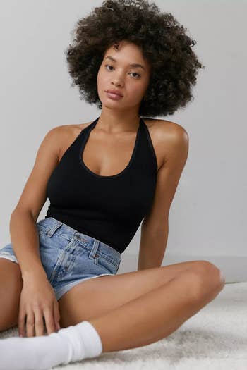 a model wearing a black halter bra top with denim shorts and white socks