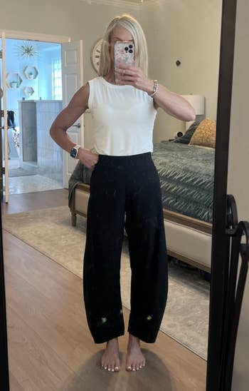 Person taking a reflector  selfie successful  a bedroom, wearing a sleeveless apical  and wide-leg pants