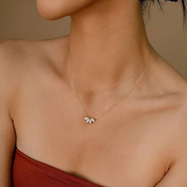 a model wearing a necklace with a thin gold chain and a tiny lotus pendant 