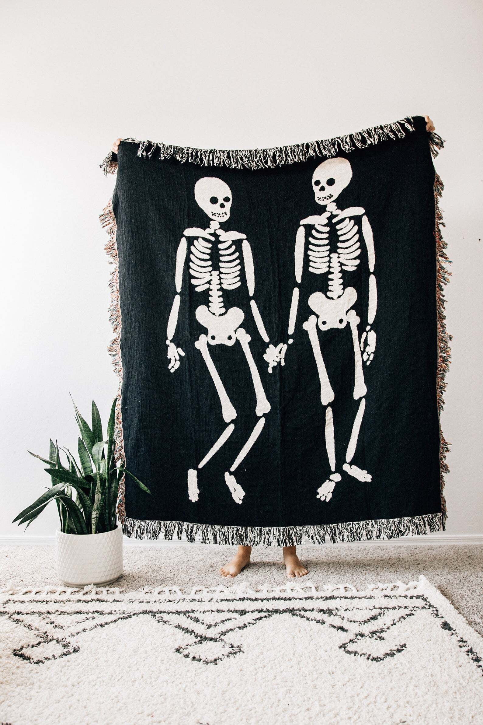 woven throw rug in black with tassels and two skeletons printed on the front