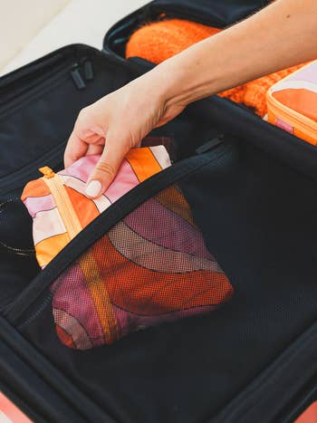 hand putting the folded up bag into a suitcase, showing how compact it is