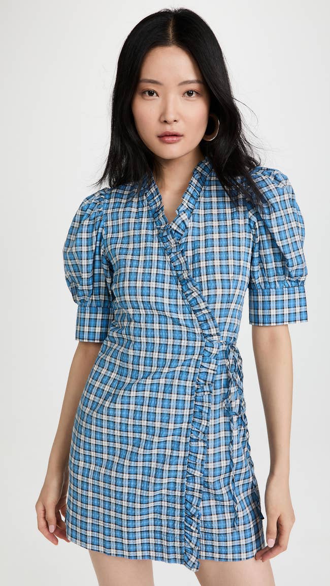 model in short sleeve mini blue plaid dress with puffed sleeves, ruffle detail, and side tie design