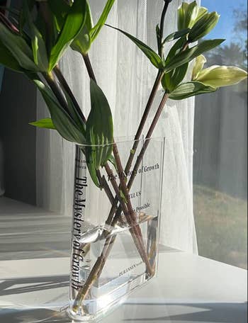 A clear book-shaped vase with flowers coming out of it 