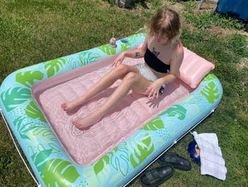 Person relaxing successful  a tiny  inflatable lounger with printed leafage  designs, wearing a strapless apical  and shorts, adjacent   sandals and a towel connected  grass