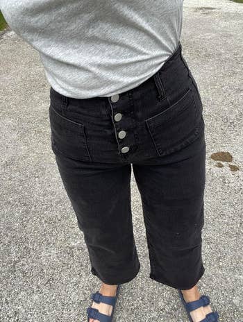 Person in a gray top and black buttoned high waist jeans 
