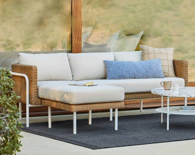 Stylish outdoor patio set with a wicker sofa and white cushions, featuring a blue and beige accent pillow, set beside a round coffee table
