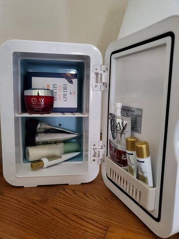 Reviewer showing the inside of the fridge and how many beauty products it can fit inside

